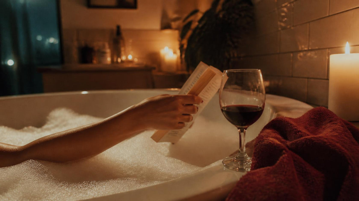 A satin gloved hand holding a card that reads Read between the sheets over an open spicy romance book